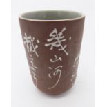 A Japanese brush pot, the brown exterior with rows of calligraphy, the interior celadon glazed,
