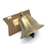 A brass bell, with iron clanger, brass bracket and shaped wooden backplate. (Dimensions: The bell