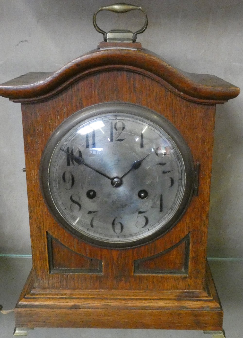 An oak cased mantle clock on raised brass feet with brass handle to top