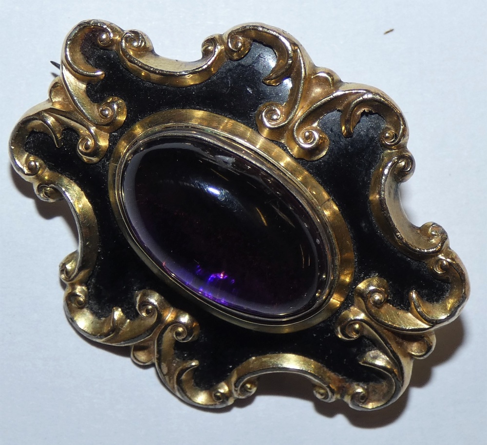 A Victorian gold, black enamel brooch set with a cabochon amethyst