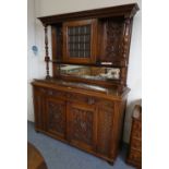 An oak sideboard with carved pediment over central glazed cupboard with carved side panels and
