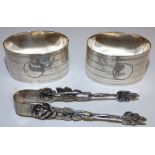 A pair of silver napkin rings, Birmingham 1929 and a pair of German silver sugar tongs, box (3)