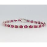 An 18ct white gold colour treated ruby and diamond line bracelet, the rubies approx. 13.3ct, the