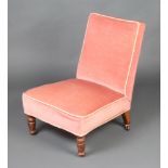 A Victorian nursing chair upholstered in rose pink material, raised on turned supports