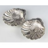 A pair of Victorian silver shell shaped butter dishes with repousse floral and scroll decoration