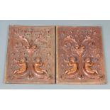 A pair of carved walnut panels decorated cherubs beneath an urn of fruit 38cm x 28cm