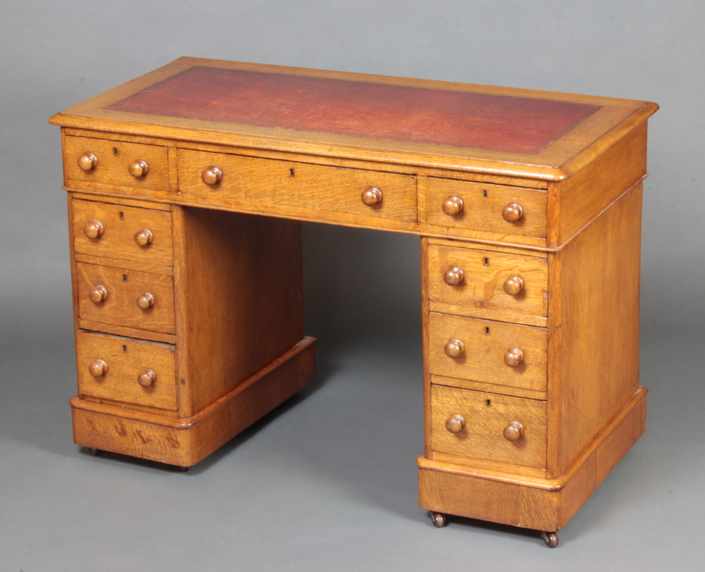 A Victorian light oak kneehole pedestal desk with inset writing surface above 1 long and 8 short