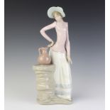 A Nao figure of a lady standing beside a plinth with a ewer 35cm