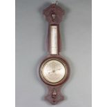 An aneroid barometer and thermometer with silvered dial contained in a carved oak wheel case