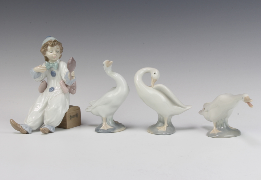 A Lladro figure of a seated boy clown 15cm together with 3 Lladro geese