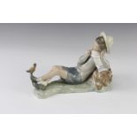 A Lladro figure of a boy resting against a log with a bird on his foot 23cm