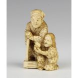 A Meiji period Japanese carved ivory okimono of a standing man with a child kneeling at his feet