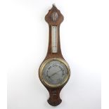 A 1930's aneroid barometer and thermometer with silvered 20cm dial, contained in a carved oak