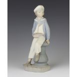 A Lladro matt figure of a boy sailor holding a toy boat, sitting on a capstan 23cm