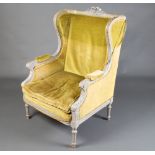 A French style winged armchair upholstered in yellow material, raised on turned and fluted