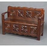 A 1920's carved oak settle with panelled back, the seat with hinged lid 84cm h x 182cm w x 41cm d
