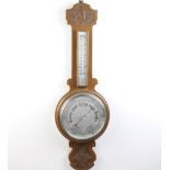 A 1930's aneroid barometer with 20cm silvered dial contained in a carved oak case (top to