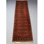 A red ground machine made Afghan style runner with 13 stylised diamonds to the centre within a multi