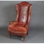A Georgian style winged armchair upholstered in red leather and raised on outswept supports There is