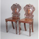 A pair of Victorian carved mahogany shield back hall chairs with solid seats, raised on turned