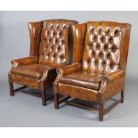 A pair of Georgian style winged armchairs upholstered in brown buttoned leather, raised on square