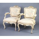 A pair of cream and gilt painted French open arm salon chairs, the seats and backs upholstered in