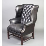 A Georgian style winged armchair upholstered in black buttoned leather, raised on square supports