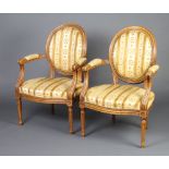 A pair of French walnut open arm salon chairs with upholstered seats and backs raised on turned