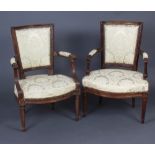 A pair of 19th Century French carved walnut open arm salon chairs, the seats and backs upholstered
