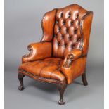 A Georgian style winged armchair upholstered in brown leather, raised on cabriole supports There