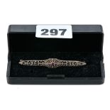 A 10K WHITE GOLD FILIGREE BAR BROOCH set with a central ruby, stamped 10k, approximately 2.5 grams.