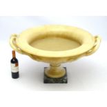 A large yellow marble kylix shaped urn on a squared green marble base ,