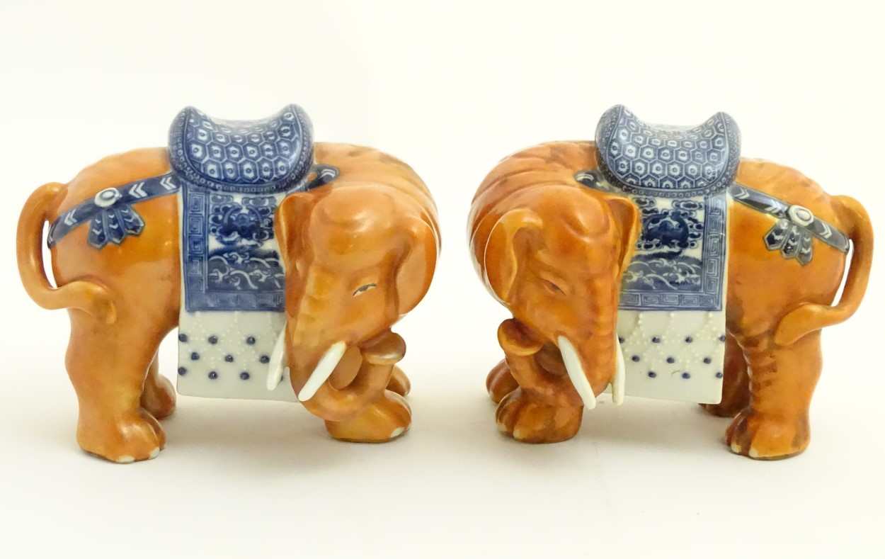 A pair of Chinese ceramic elephants with rust coloured bodies and blue and white patterned saddles.