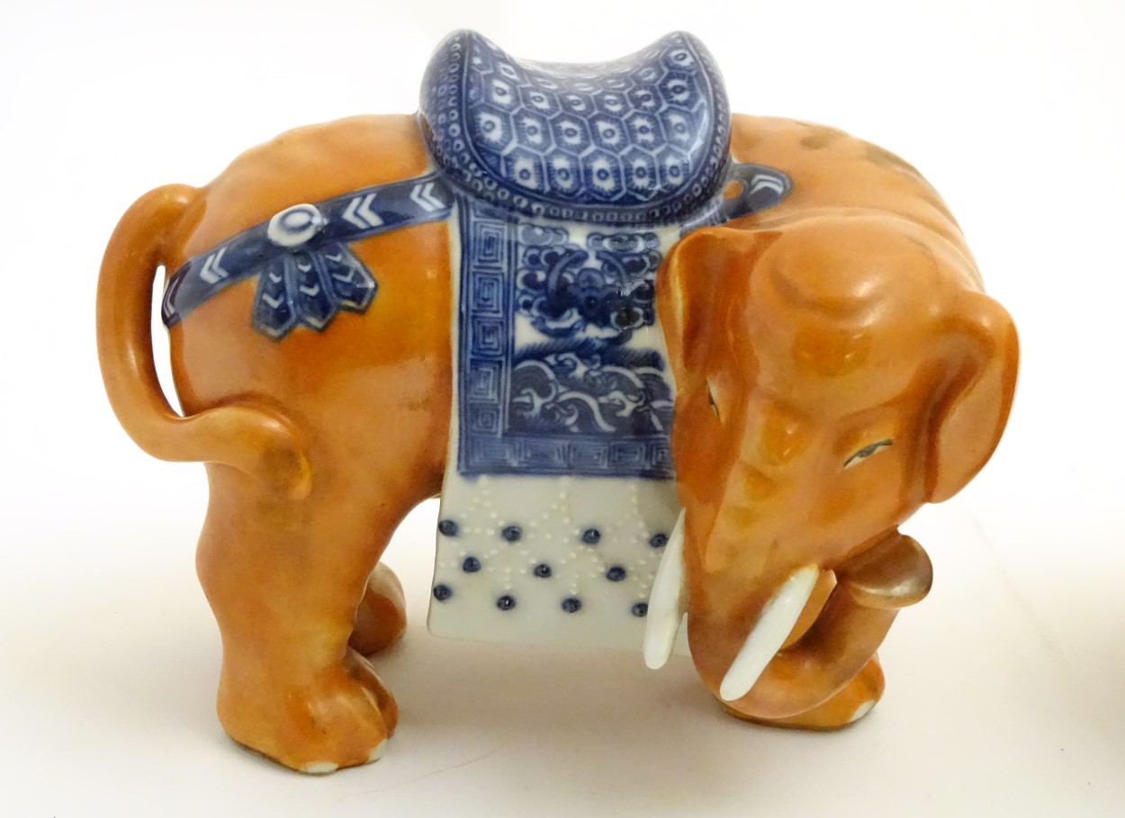 A pair of Chinese ceramic elephants with rust coloured bodies and blue and white patterned saddles. - Image 2 of 7