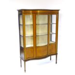 An early 20thC mahogany serpentine fronted display cabinet having feather banded veneering and