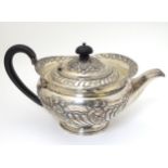 A large silver teapot with embossed decoration and ebonised handles.