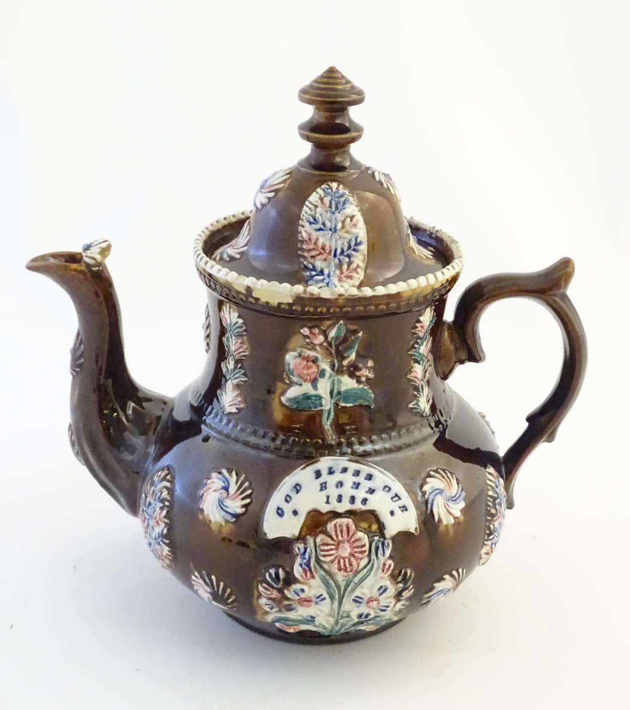 A late 19thC Measham bargeware teapot and cover with floral decoration surrounding a plaque