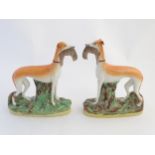 A pair of 19thC flatback Staffordshire greyhounds holding rabbits in their mouths on oval bases.