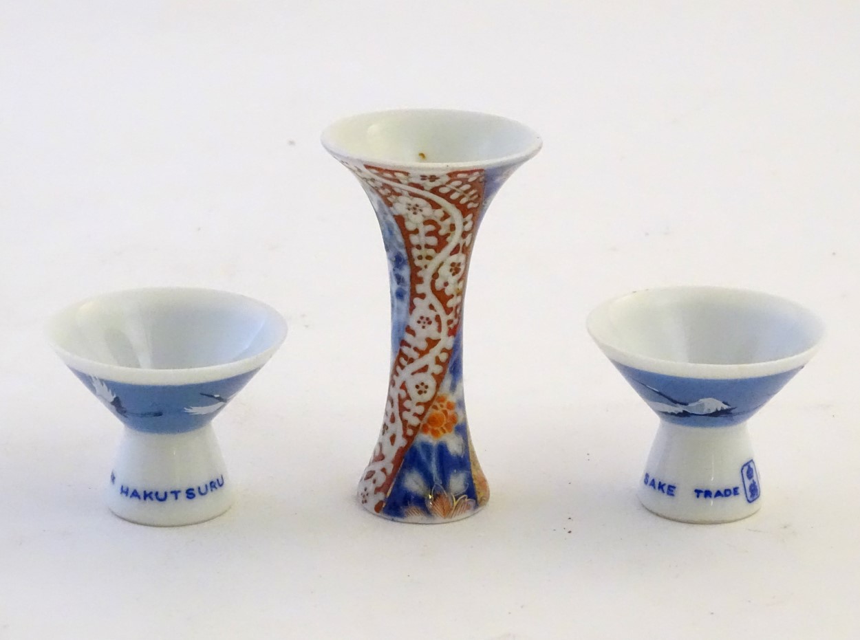 A pair of Japanese porcelain sake cups advertising Hakutsuru, decorated with flying cranes.