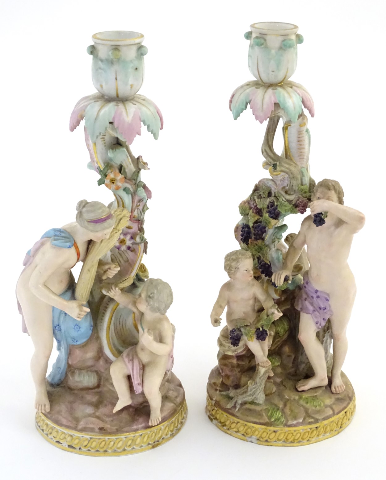 Two Meissen porcelain candlesticks, one depicting Bacchus and a child with vines and grapes,