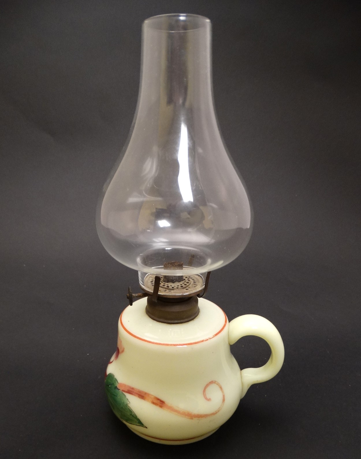 A small glass oil lamp with floral decoration, loop handle and clear glass chimney.