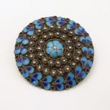 A silver brooch of circular form decorated with turquoise and blue enamel decoration.