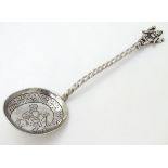A white metal spoon with engraved bowl and twist handle surmounted by a deity / Buddha.