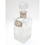 A cut lead crystal decanter of squared form with silver collar and with silver wine label /
