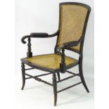 A late 19thC ebonised caned seated open armchair with leather upholstered manchettes,