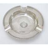 A silver ash tray with engraved crossed golf club emblem titled AGC.