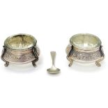 A pair of Continental white metal salts with floral scroll decoration and clear glass liners.