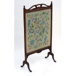 An early 20thC oak fire screen with a shaped handle and having a needlework interior.