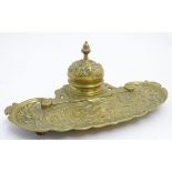 Standish / Inkwell: a cast brass desk piece having a hinged inkwell and a relief decorated pen tray