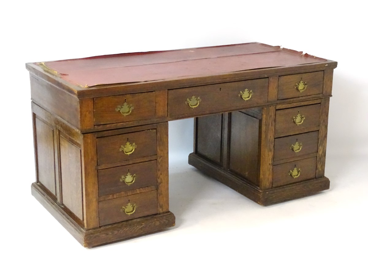 An early 20thC oak pedestal desk comprising a single long central drawer flanked by four short